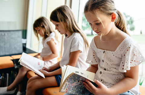 Three preschool girls reading books in the library
