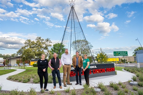 People standing in front of sign and christmas tree in park.jpg